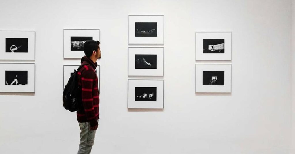 A man stands in an art gallery, observing framed black and white photographs.